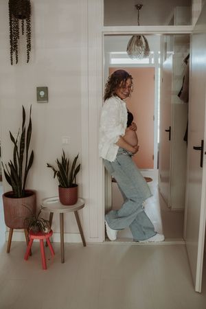A series of photos showing someone in a blue dress tending to indoor plants on pink stools in a minimalist white space.