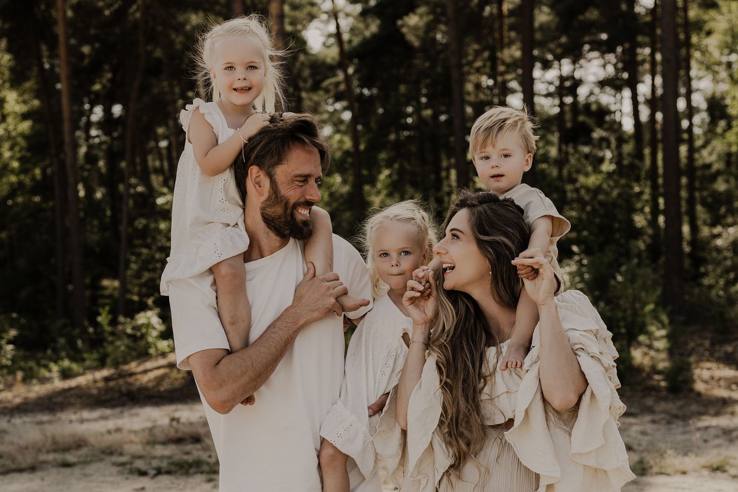 Joyful family with three young children in beige outfits in a pine forest.