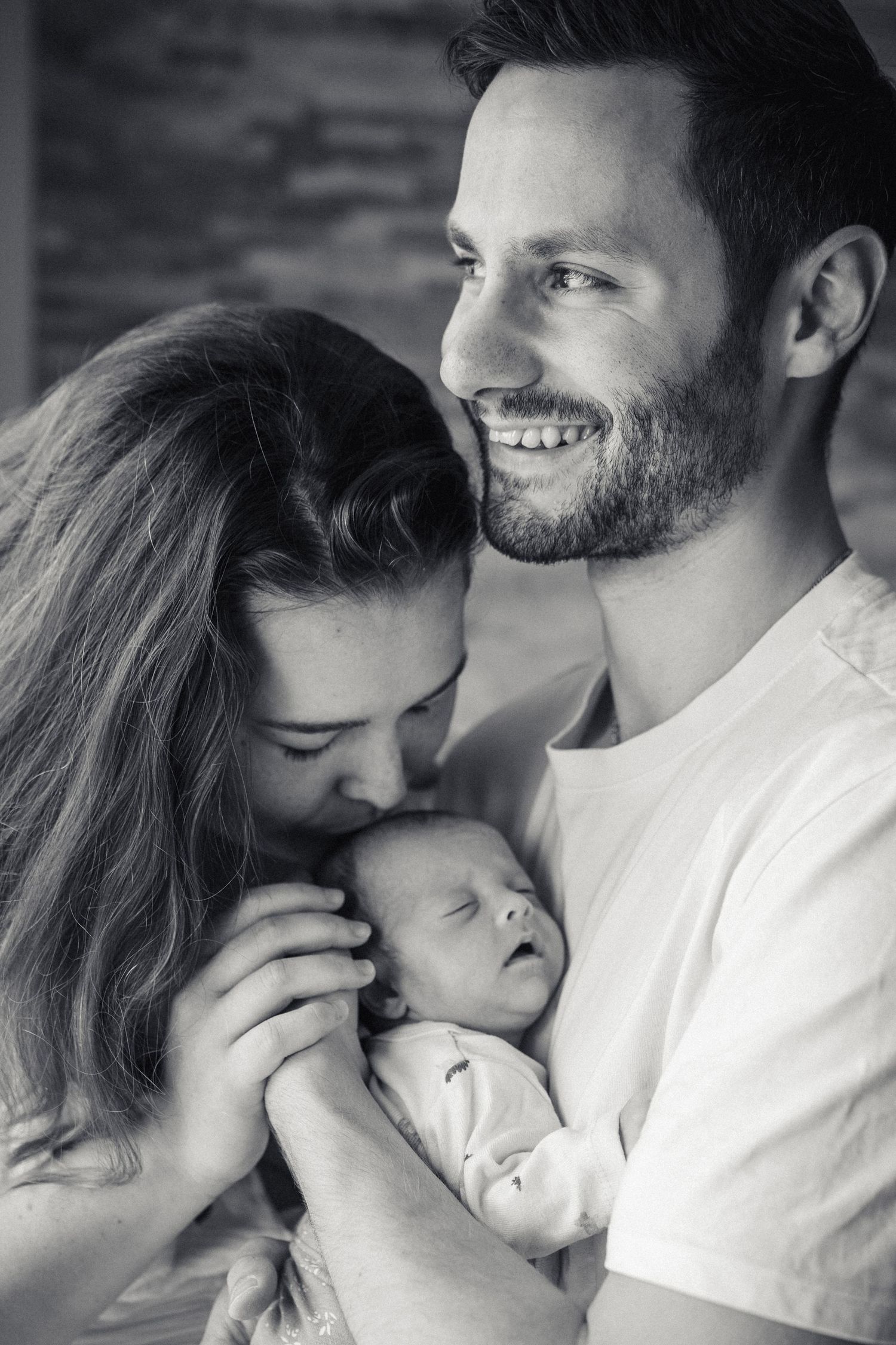 A tender moment captured at the beach as a parent holds a baby in soft neutral clothing against a coastal backdrop.