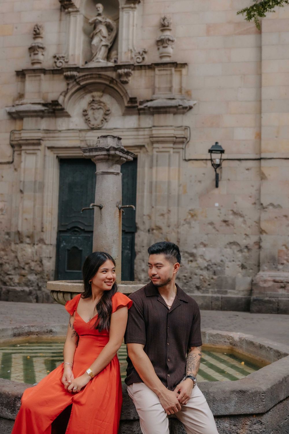 Wide shot of couple in front of historic architecture in Barcelona Old City for engagement announcement.