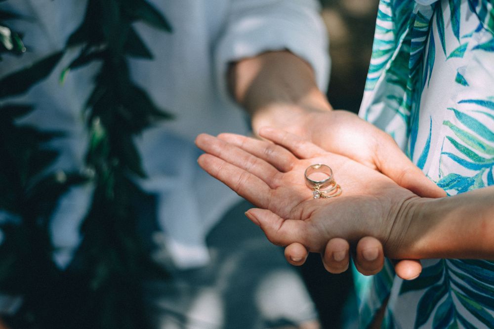 Close-up of hands holding a wedding ring against a backdrop of tropical print clothing.
