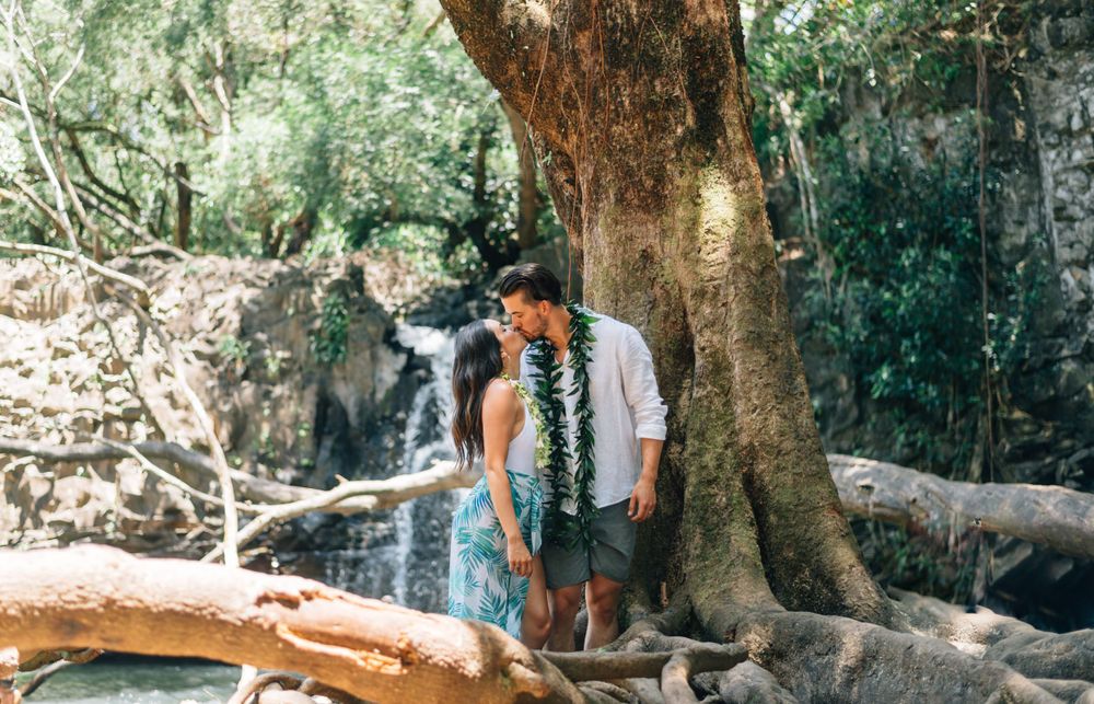 A couple poses together near a waterfall in a tropical forest setting.