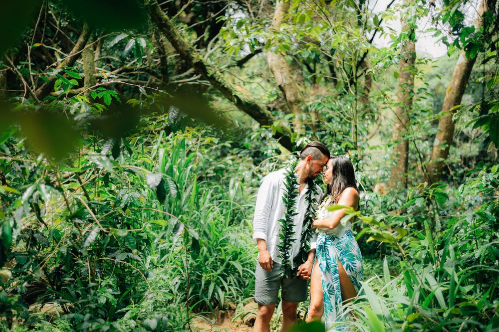 A couple shares a tender moment on a forest path surrounded by lush tropical vegetation.