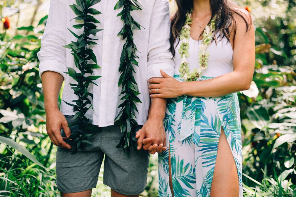 Close-up of a couple holding hands while wearing tropical print clothing and black lei necklaces.