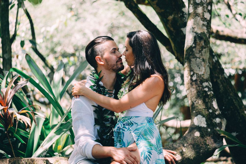 A couple embraces in a lush tropical garden setting wearing traditional Hawaiian leis.