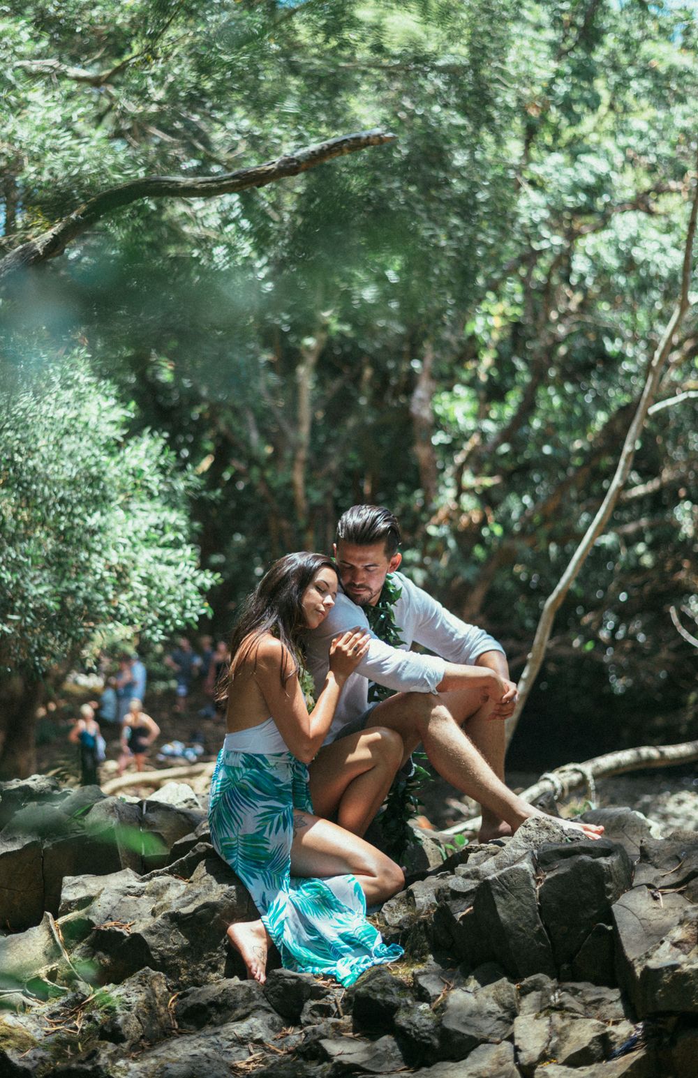 A couple shares a romantic moment on rocky terrain in a tropical forest setting.