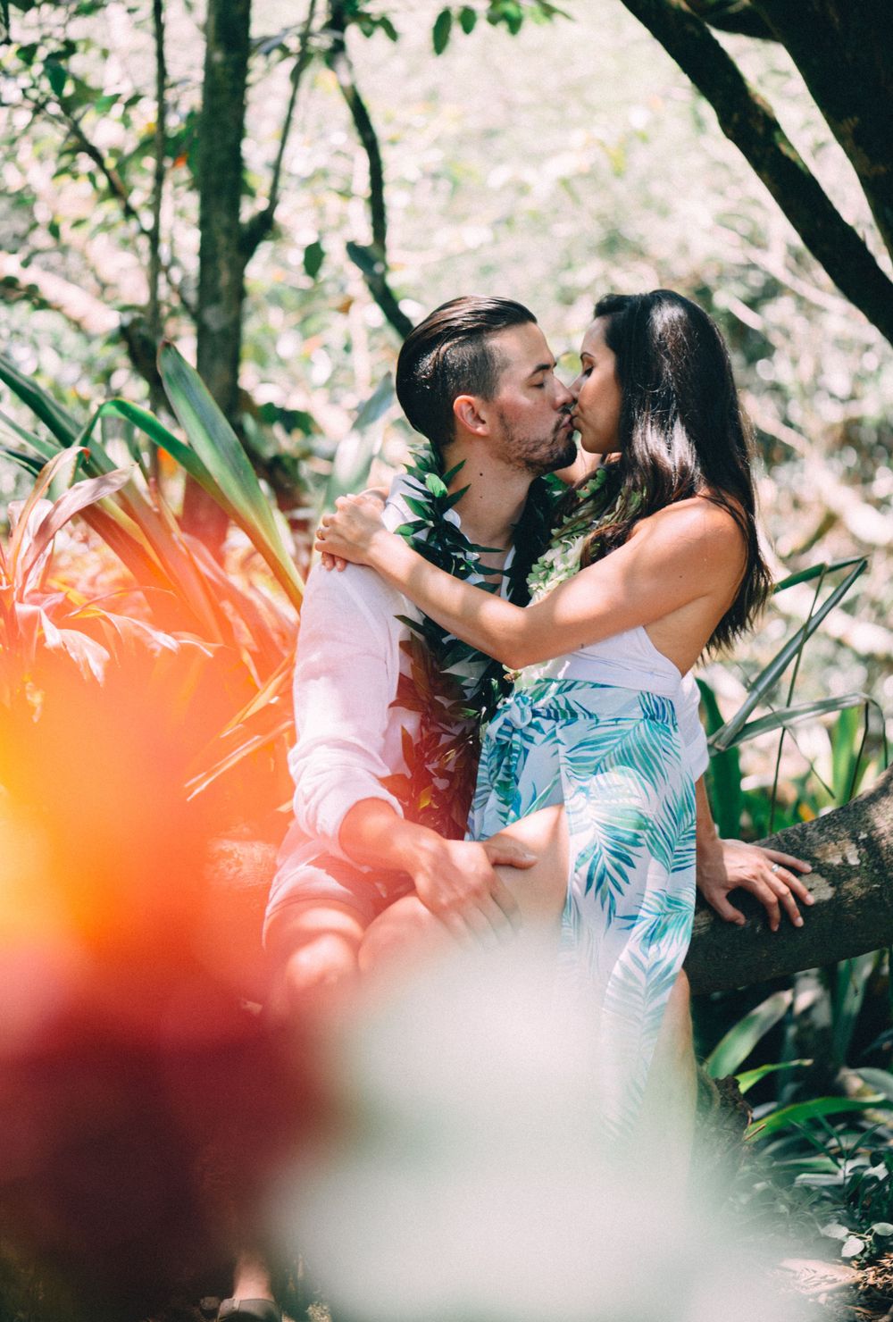 A romantic kiss captured through leaves with warm orange light effects.