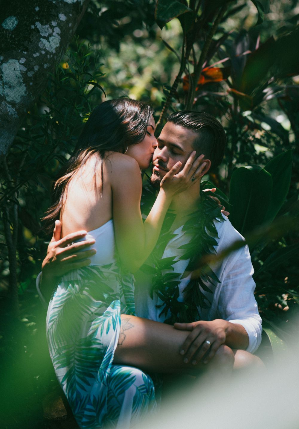 An intimate moment between two people partially hidden by lush green foliage.
