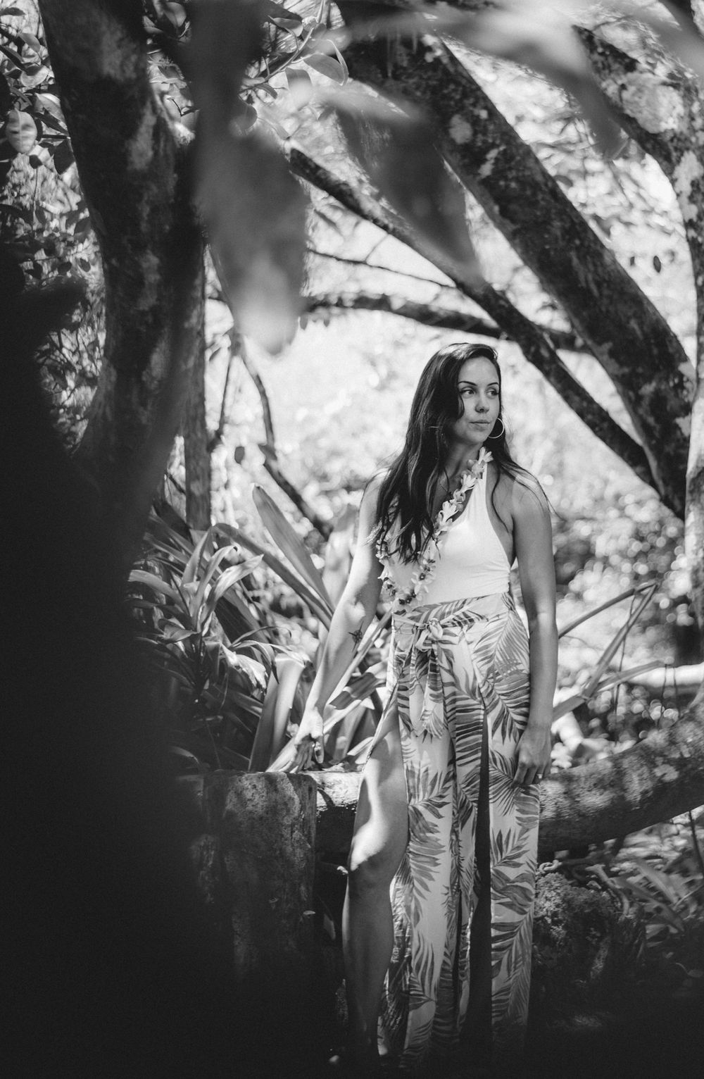 A person in a tropical print dress poses against a black and white forest backdrop.