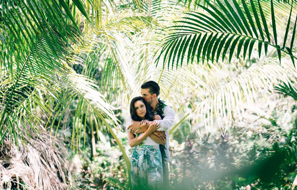 Couple embracing in a sunlit tropical garden with palm fronds in the background.