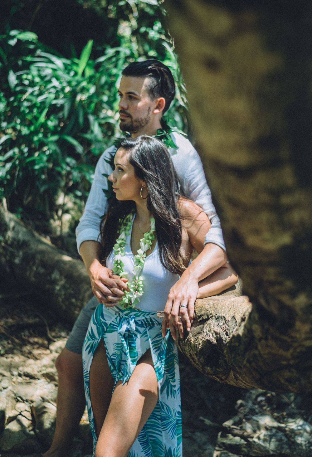 A couple shares an intimate moment on rocky terrain surrounded by tropical plants.