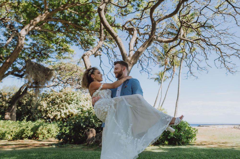 Wedding couple embraces in a scenic outdoor location with palm trees and ocean views.