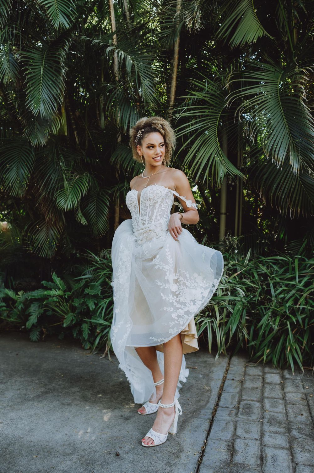 Elegant white lace wedding dress detail shot in a tropical garden setting.
