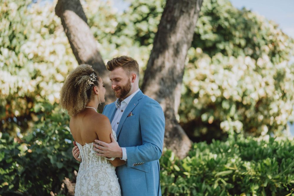 Romantic couple shares an intimate moment under lush green trees in a tropical garden setting.