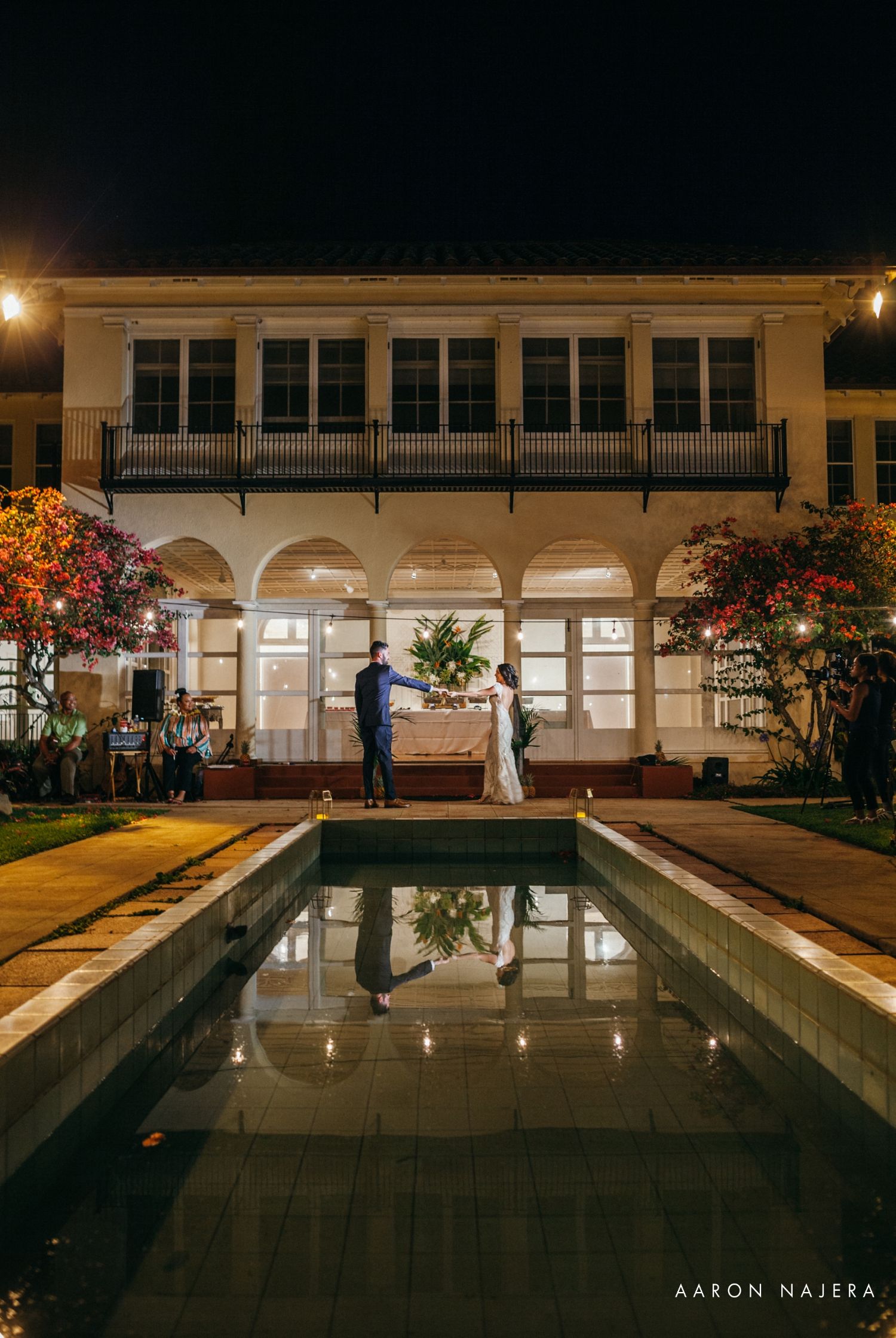 Elegant wedding venue at night with illuminated pool reflecting a colonial-style building with arches.