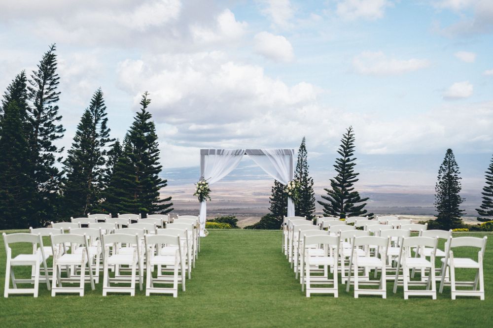 Outdoor wedding ceremony setup with white chairs and arch overlooking mountain landscape.