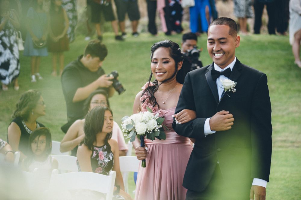 Wedding party members walking in pairs down a grassy outdoor aisle.