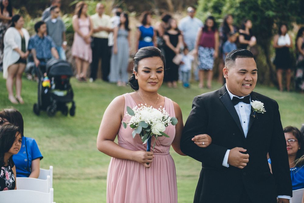 Wedding guests seated in white chairs on a grassy lawn during an outdoor ceremony.