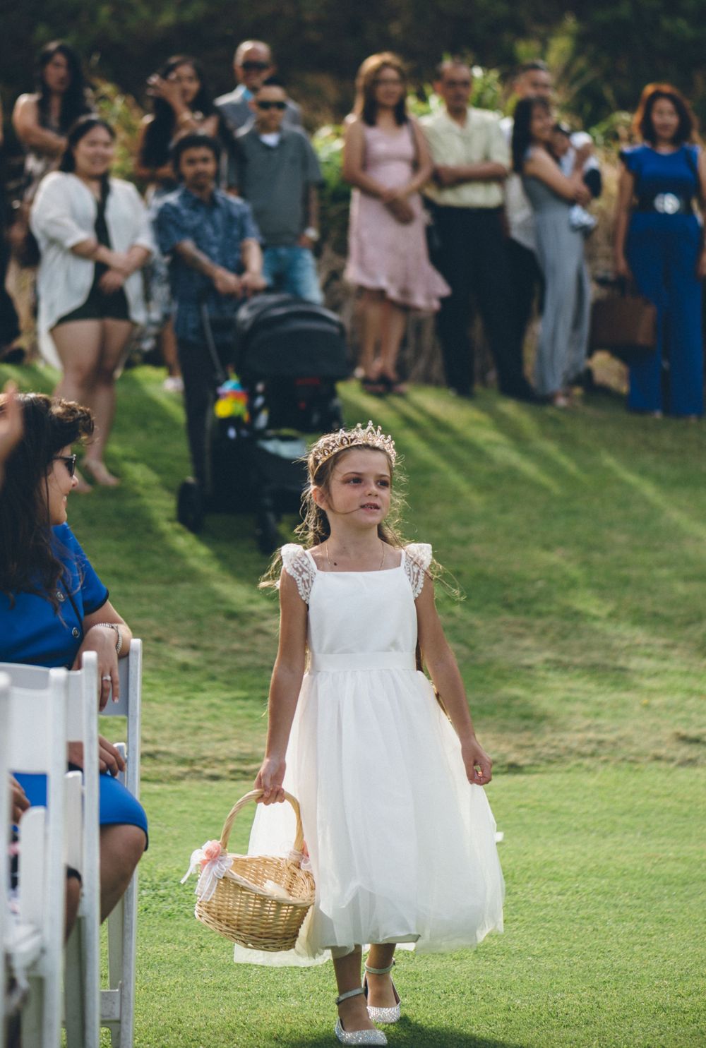 Young flower girls in white dresses walking down the aisle carrying baskets.