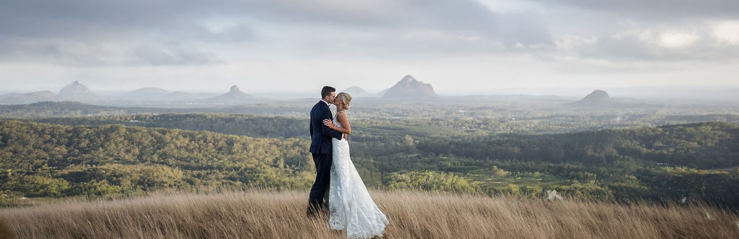 Bride and groom embrace on a hilltop with breathtaking panoramic views of the Glasshouse Mountains.