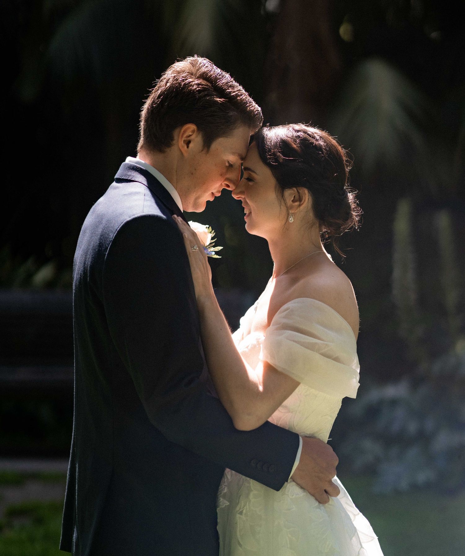 A couple in wedding attire share an intimate dance outdoors with soft lighting creating a romantic silhouette.