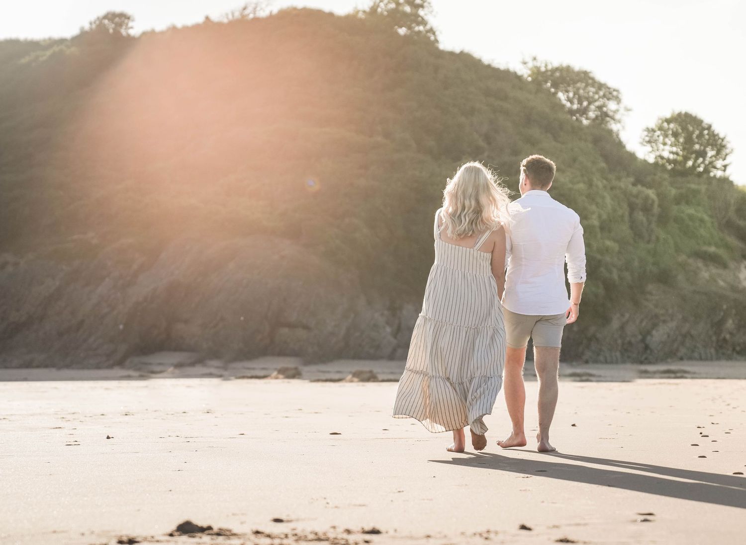 Two people walking together on a sandy beach at sunset with cliffs in the background.