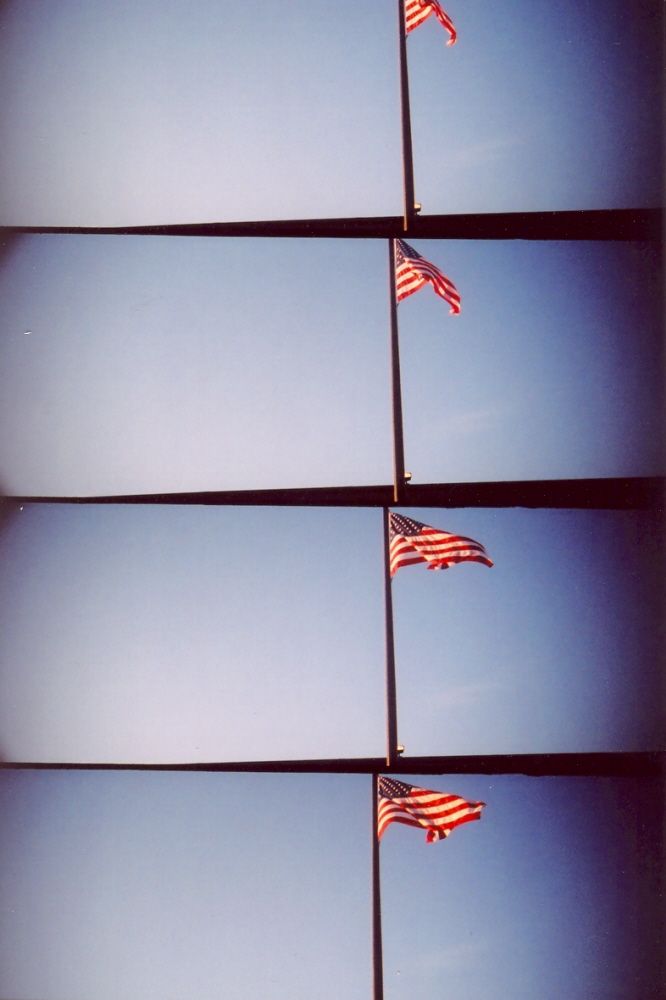 Multiple American flags wave against a blue sky with geometric architectural lines creating a modern abstract composition.