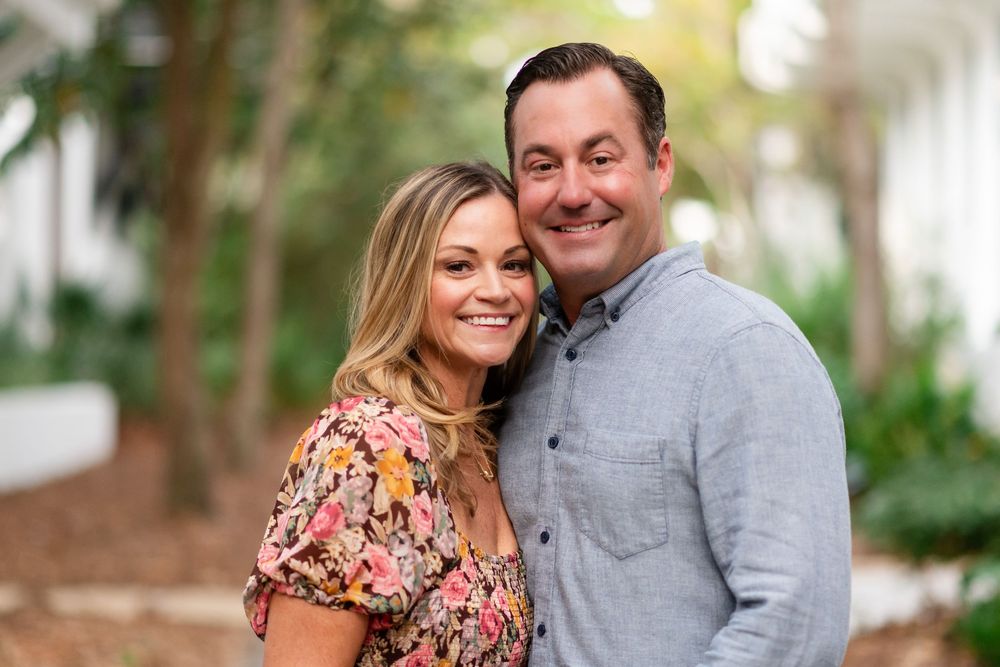 Couple in coordinated outfits posing together outdoors with trees and natural scenery behind them.