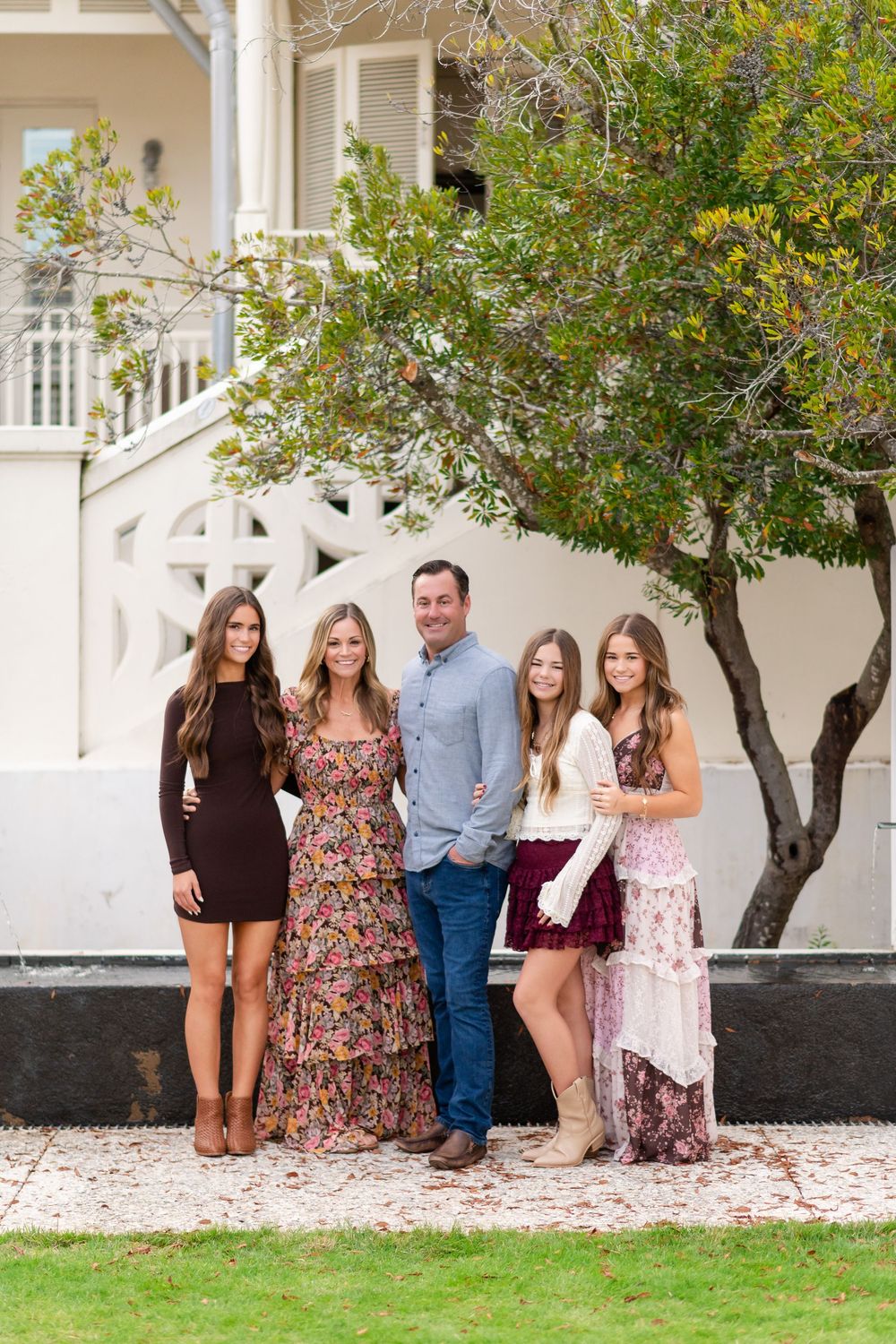 A group stands together in front of a white building with trees and landscaping in a progression of casual poses.
