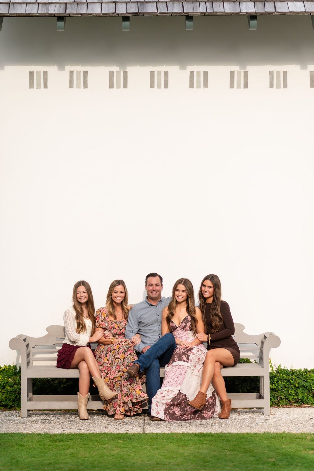 A group sits together on a gray bench against a white wall with architectural details.