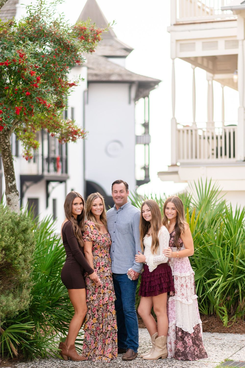 A group poses together outdoors against a white building with tropical landscaping and palm plants.