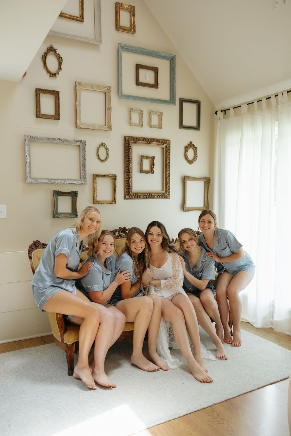 A group wearing matching blue outfits sits together in a room decorated with empty vintage frames on a white wall.