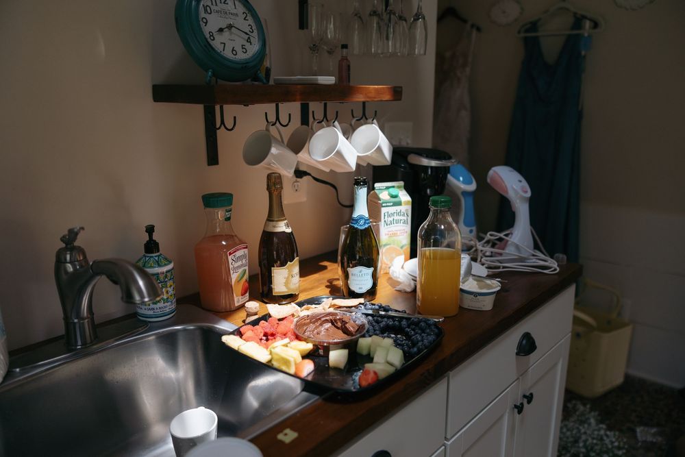 Kitchen counter with snacks, drinks, and ingredients arranged near a sink under dim lighting.