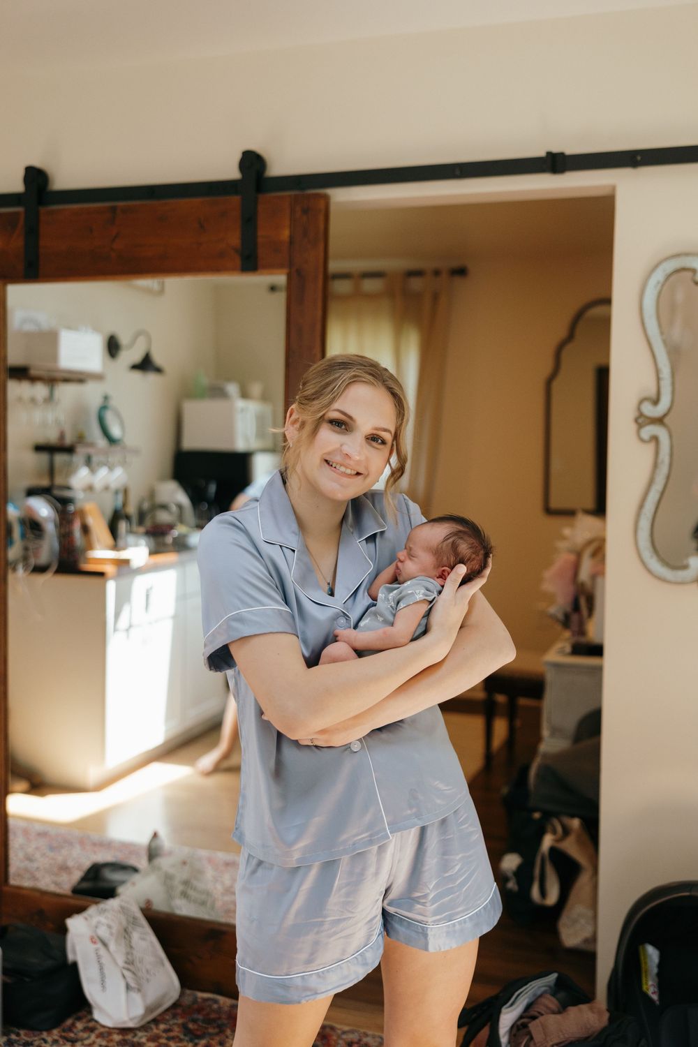A healthcare worker in blue scrubs cradles and comforts a newborn baby in a warmly lit medical setting.
