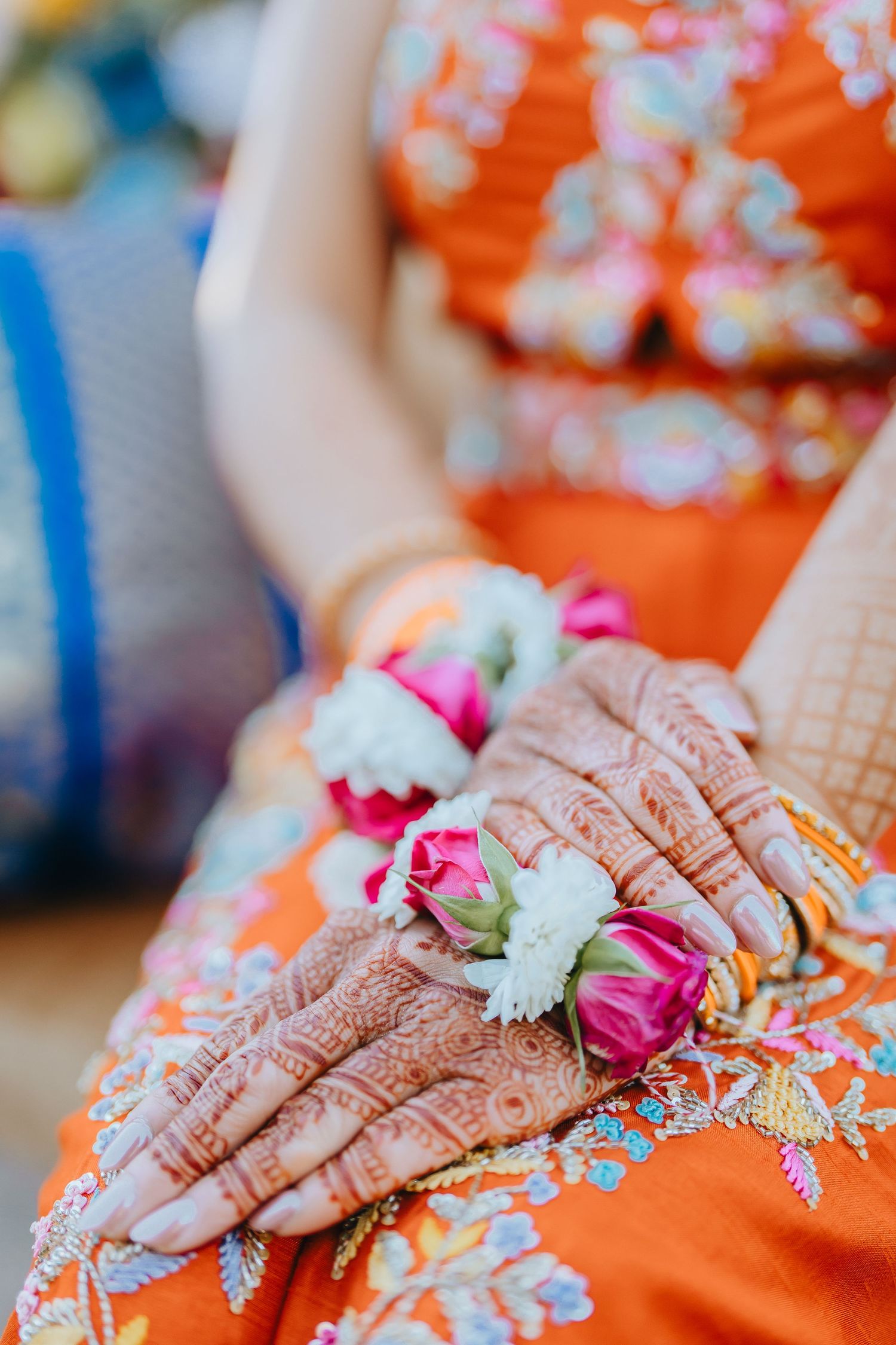 Close-up of intricate henna designs on hands with pink floral accents against orange fabric.