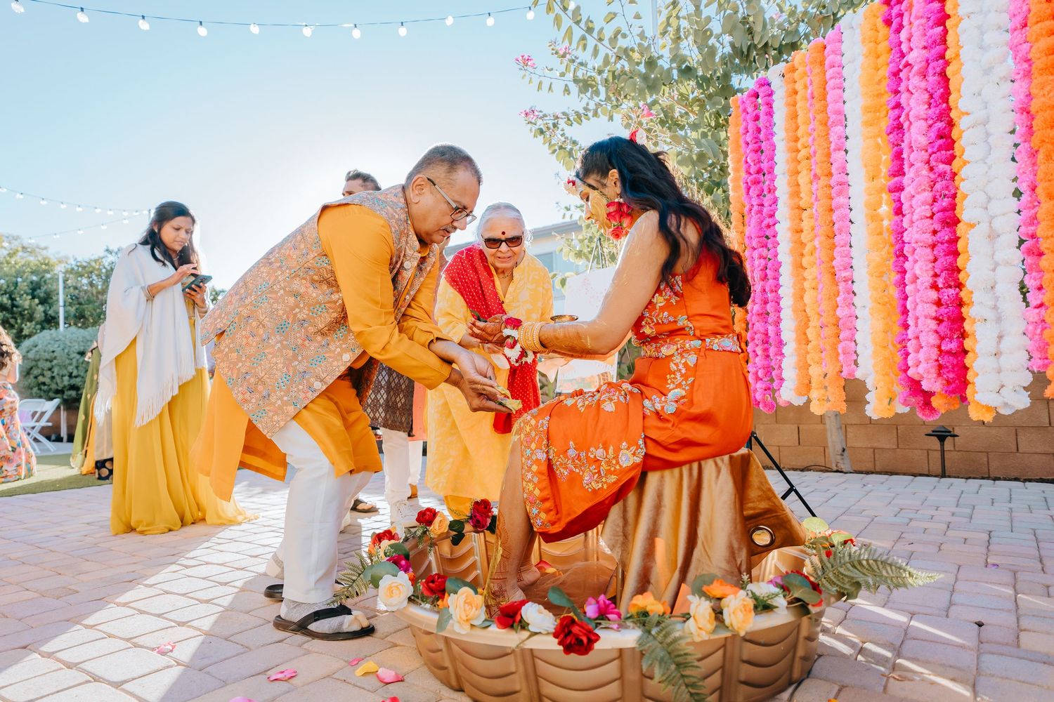 Traditional Indian wedding ceremony with yellow and orange decor and hanging floral garlands.
