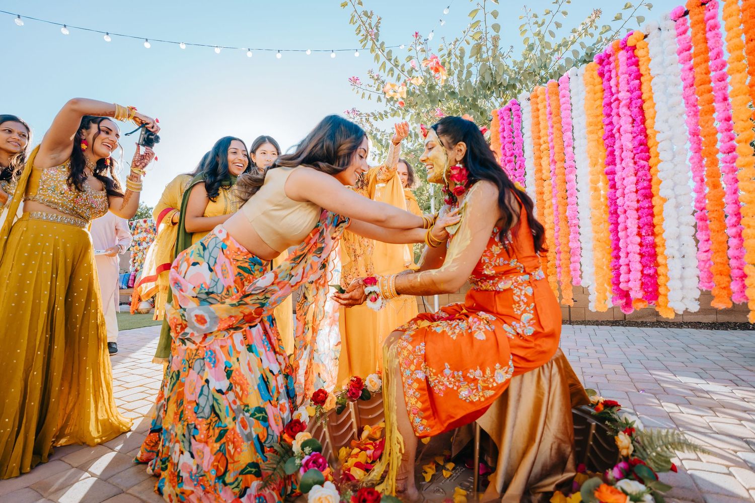 Vibrant outdoor celebration with colorful pink and orange hanging decorations and guests in festive attire.