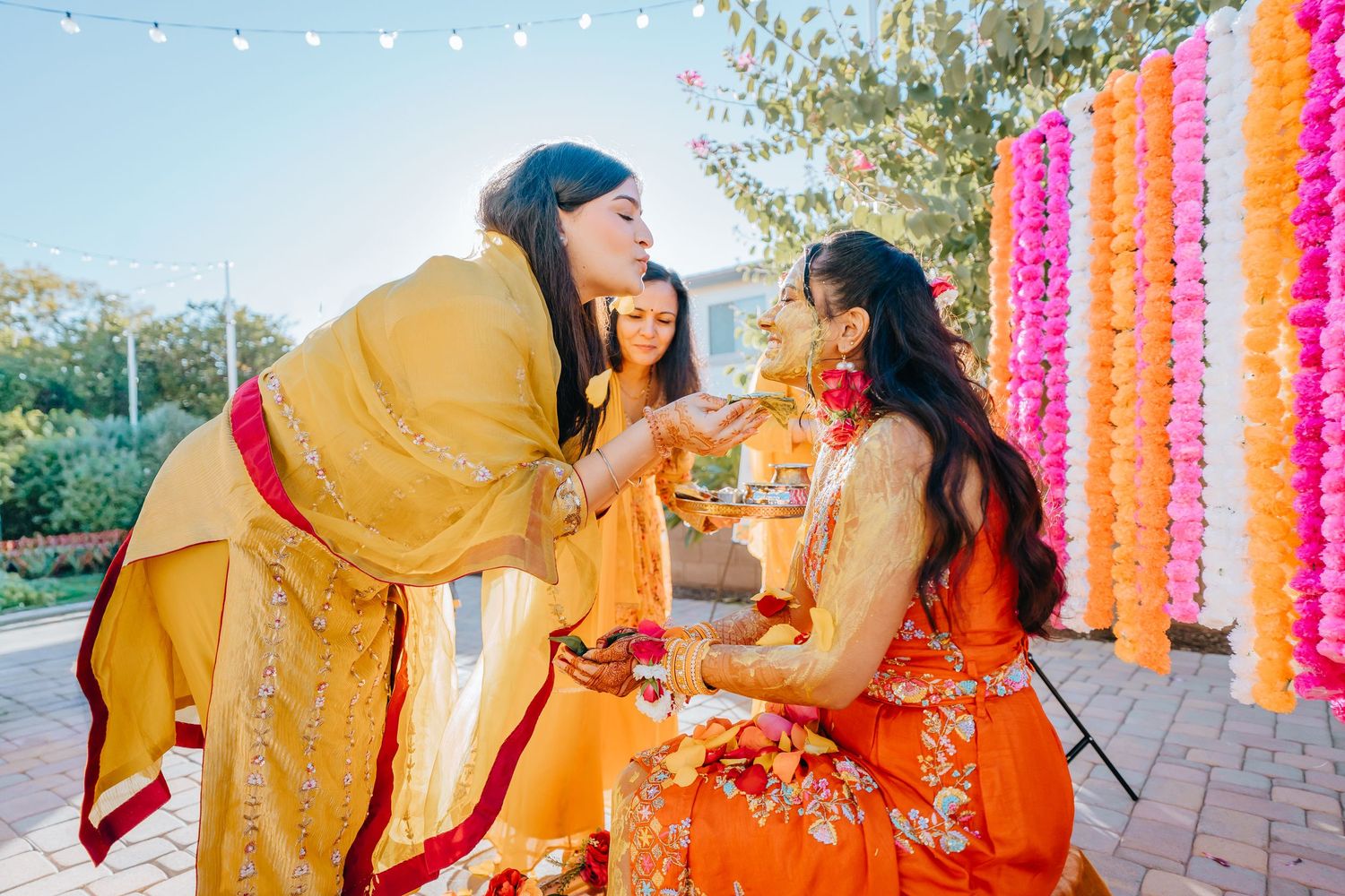 Outdoor Indian wedding celebration with bright orange and pink floral decorations and string lights.