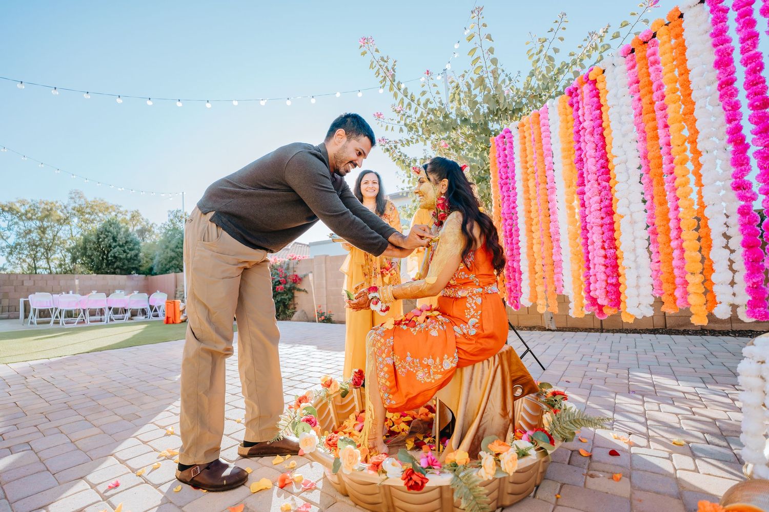 Vibrant outdoor ceremony setup with orange and pink floral decorations and hanging garlands.