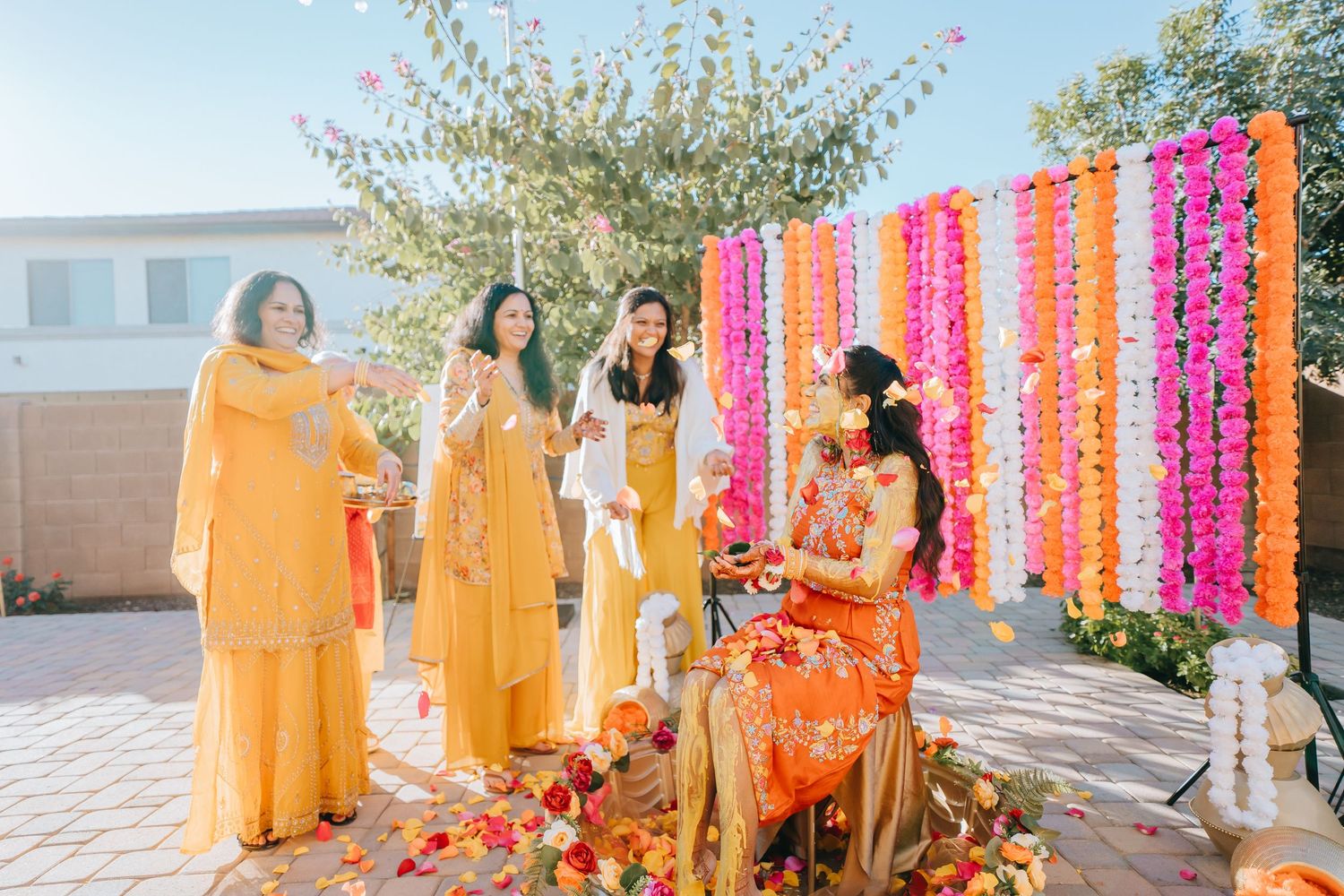 Wedding party in yellow traditional outfits posing outdoors with colorful floral backdrop.
