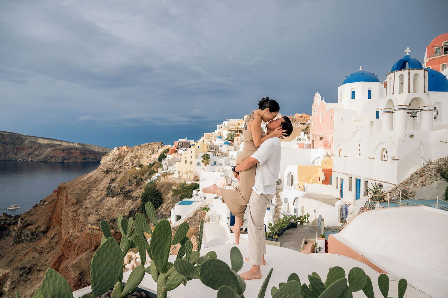 cople in front of white buildings and blue domed churches along the cliffside of Santorini, Greece