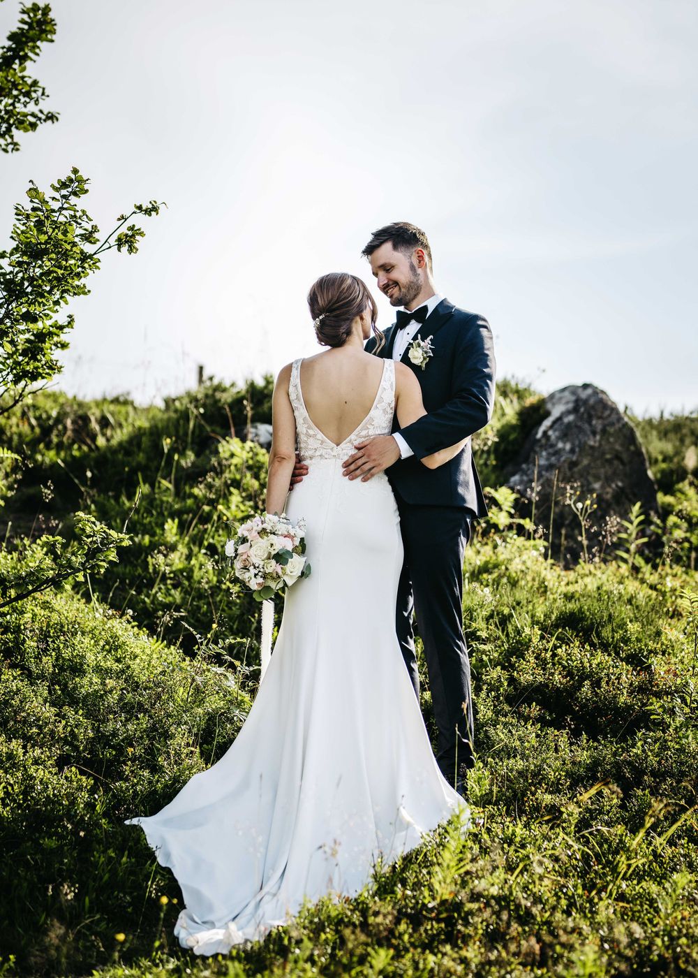 Romantic wedding couple embraces while walking through lush green garden setting on their special day.