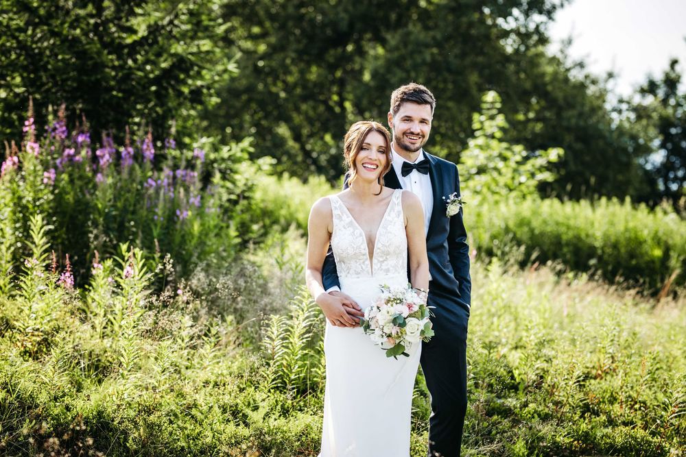 A wedding couple embraces in a lush green garden setting during their summer celebration.