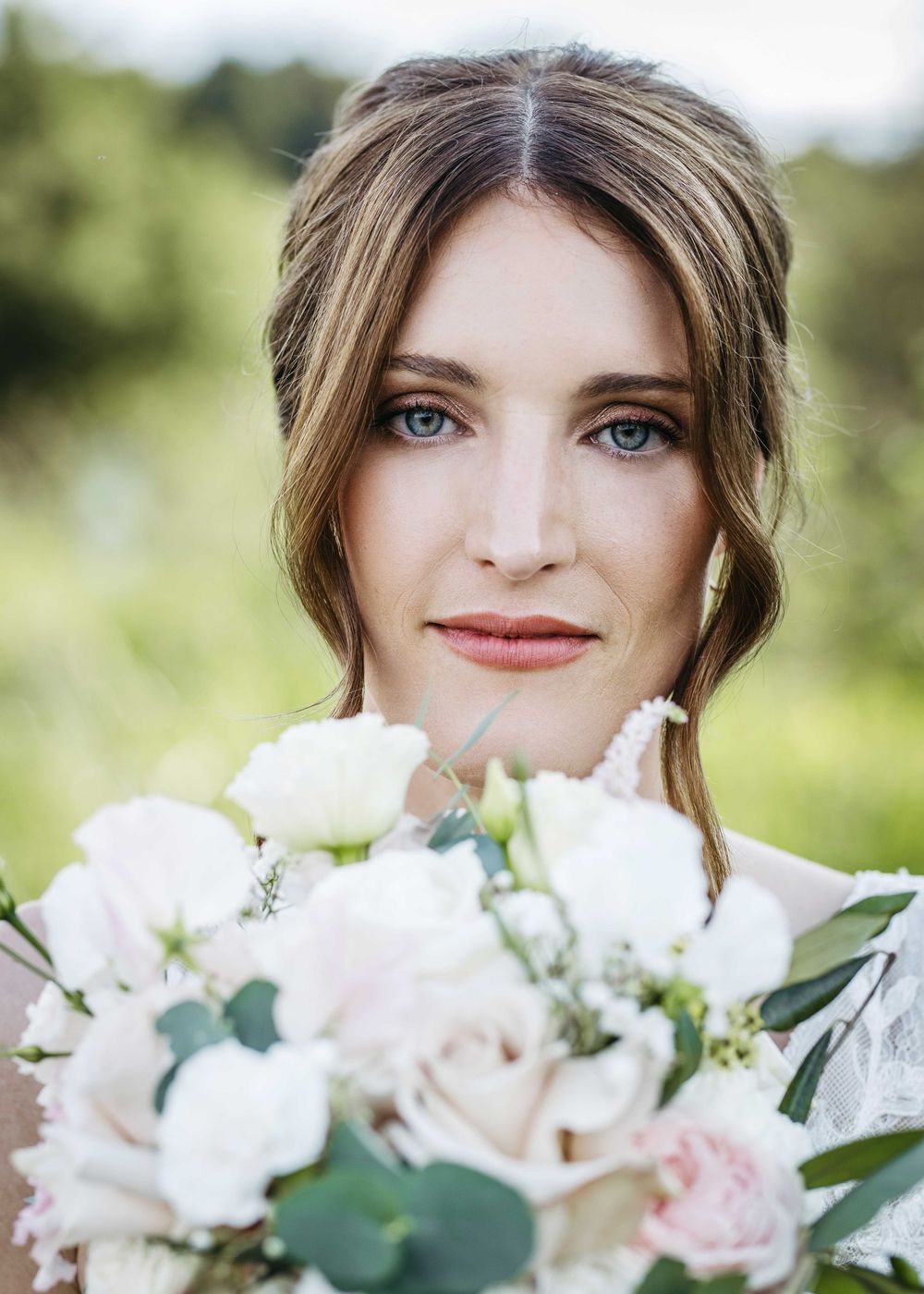 Romantic bridal portrait with delicate white flowers and soft green eucalyptus against a dreamy outdoor backdrop.