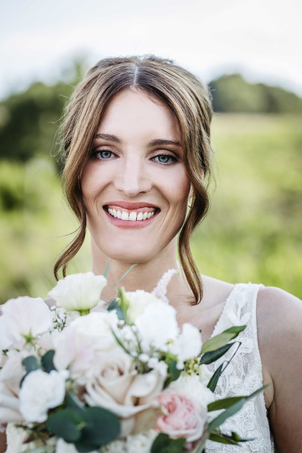 Beautiful bridal portraits with soft pink and white rose bouquet against natural outdoor backdrop.