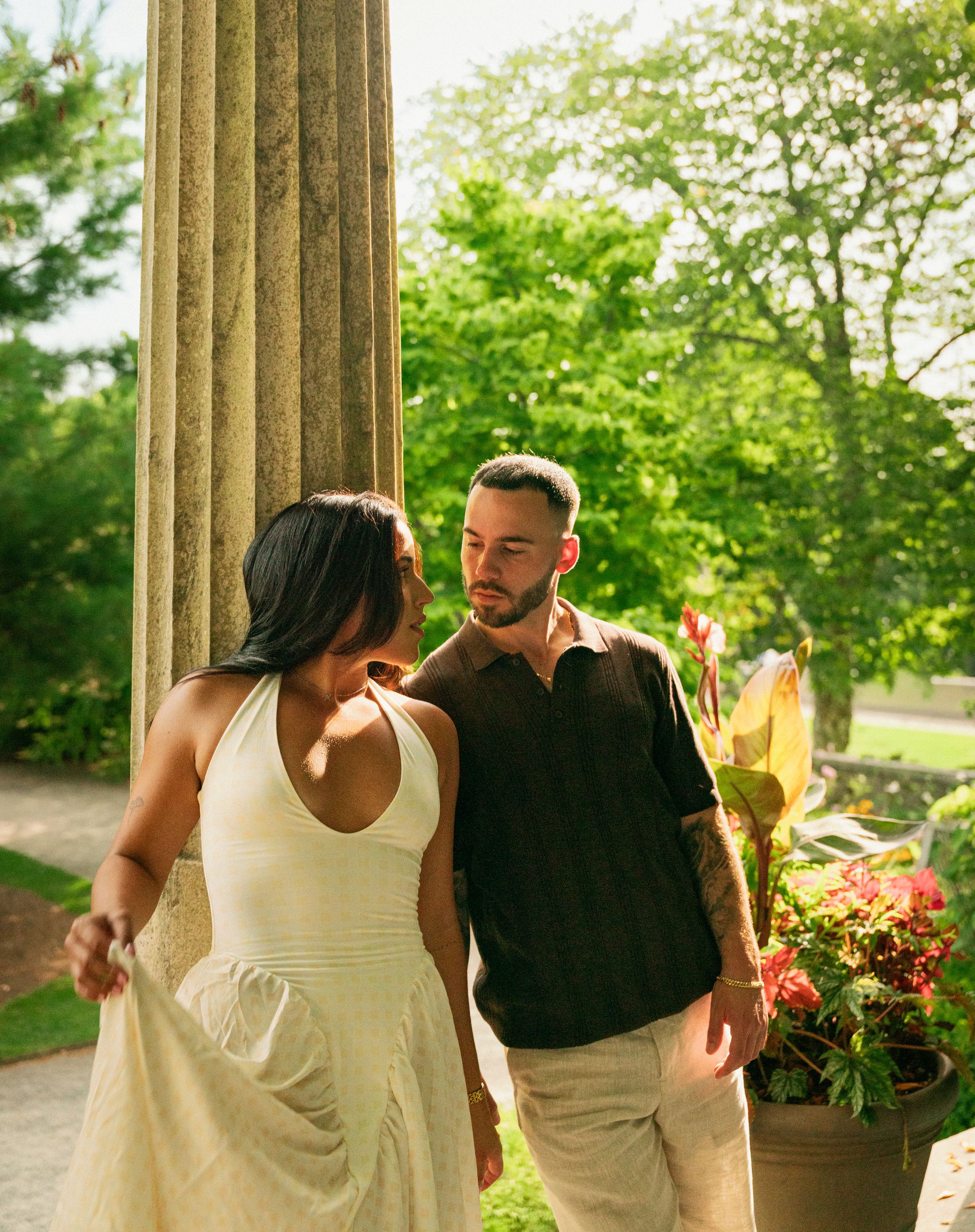 A romantic moment captured between a couple near classical stone columns in a garden setting.