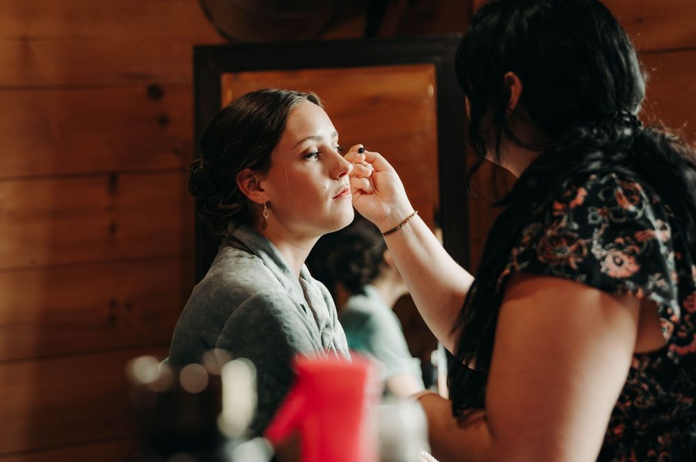Bride getting professional makeup applied in a rustic wooden bridal suite before her wedding ceremony.