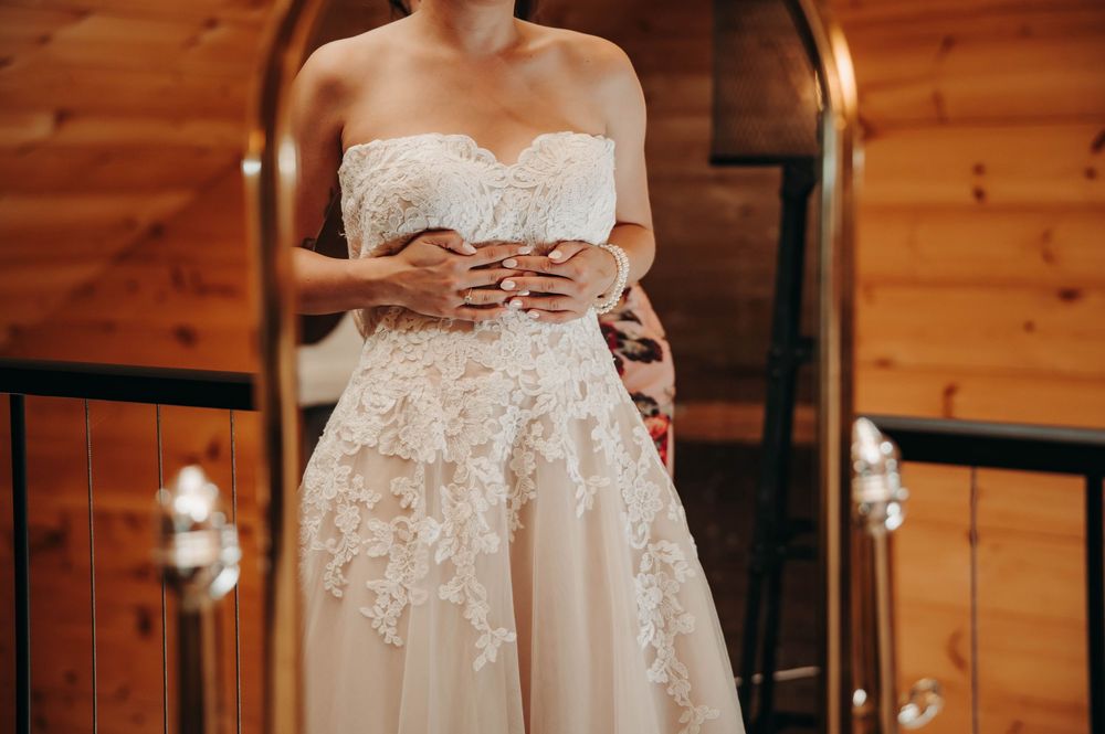 Close-up of bride in a strapless lace wedding gown holding her waist in a rustic wooden bridal suite.