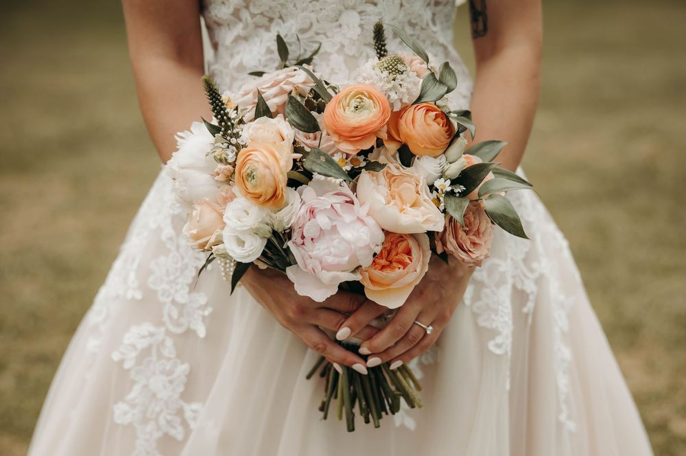 Close-up of bridal bouquet featuring peach ranunculus, blush peonies, and garden roses.
