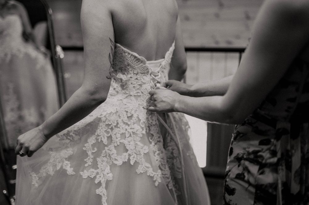 Black and white photo of a bride having her lace wedding dress fastened by a bridesmaid.